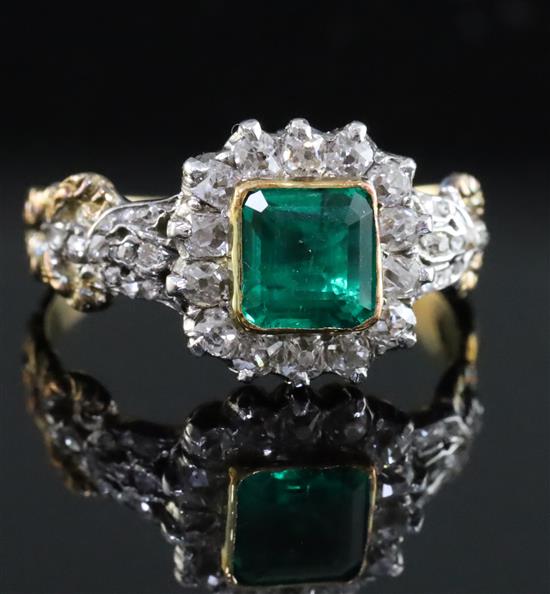 An antique 18ct gold, emerald and diamond cluster ring, the central square cut emerald (0.88ct) bordered by 14 old cut diamonds,